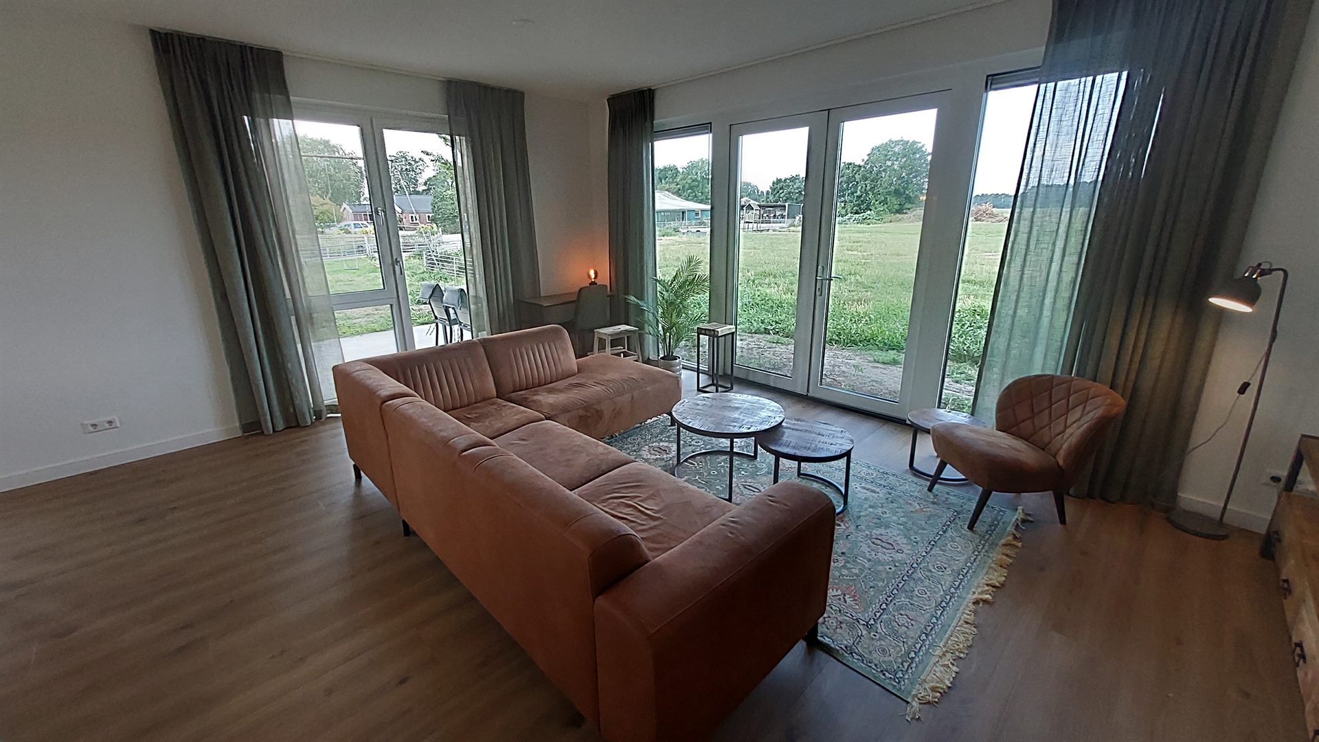 Woonkamer met hoekbank en fauteuil, openslaande deuren naar de polder