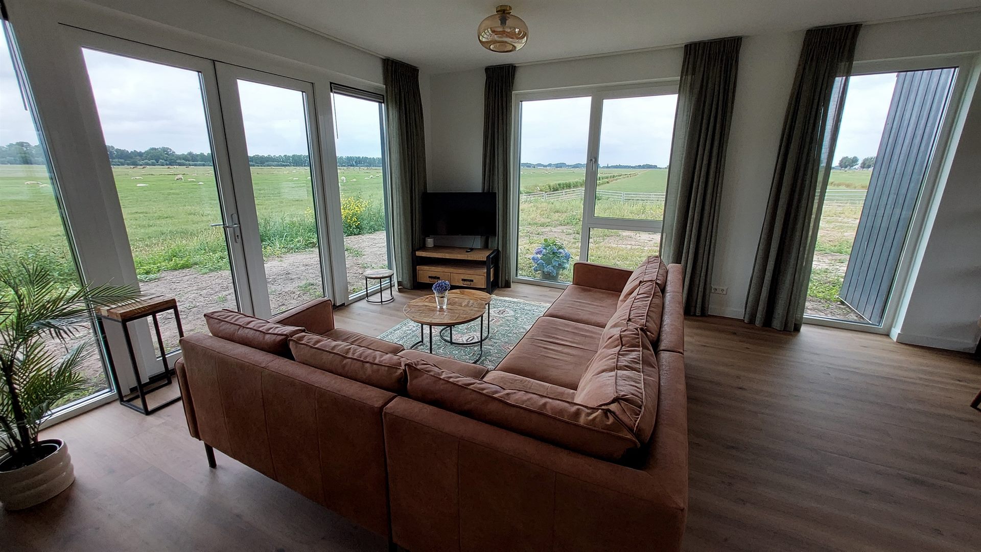 Woonkamer met hoekbank en tv, grote ramen met uitzicht op de polder